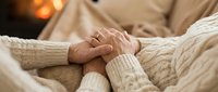 Senior couple holding hands together in cozy sweaters, expressing love and togetherness. Warm intimate moment between mature partners showing affection and emotional connection.