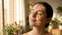 Young woman enjoying warm sunlight streaming through window creating natural shadow patterns on her face in cozy home interior for wellness and relaxation concepts.