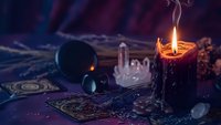 Mystical fortune telling setup with burning candle, tarot cards, crystal ball and gemstones creating atmospheric divination scene for spiritual guidance.