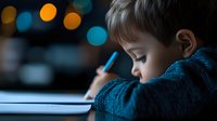 Young Caucasian boy doing homework at night, concentrated on writing in notebook with blurred bokeh lights in background, side view portrait showing focus and dedication.