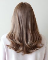 Back view of long ash blonde hair with subtle waves and layered ends styled in modern cut against neutral background, showcasing professional salon result.