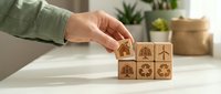 Hand arranging wooden blocks with environmental sustainability icons including recycling symbols and renewable energy concepts on white surface.