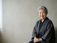 Senior Asian woman with gray hair wearing dark patterned jacket, smiling at camera against neutral background. Suitable for healthcare, wellness, lifestyle and corporate communications.