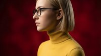 Young blonde woman in yellow turtleneck sweater and glasses profile view against red background for fashion and lifestyle concepts.