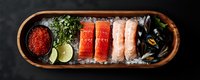Fresh seafood platter with raw salmon, tuna, caviar, mussels and lime slices served in wooden boat-shaped dish on crushed ice against dark background.