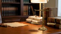 Brass scales of justice on wooden desk with law books and documents in attorney office or courtroom setting for legal consultation and judicial proceedings.