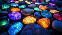 Glowing colorful stones arranged on dark surface create magical illuminated pattern with blue, orange, purple and green lights radiating through translucent minerals.