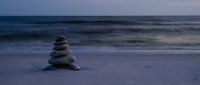 Zen stone stack on peaceful beach at twilight with soft ocean waves creating serene meditation atmosphere for wellness and mindfulness practices.