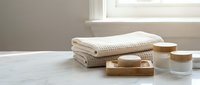 Spa wellness setup with folded towels, natural soap bars and candles on marble surface near window creating peaceful bathroom atmosphere for relaxation.