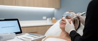 Young Caucasian woman receiving professional facial skincare treatment at modern beauty clinic with cosmetologist hands applying mask or serum.