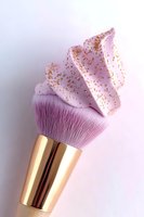 Makeup brush with pink cream and gold glitter topping styled as cupcake frosting against soft pink background, creative cosmetic art photography.