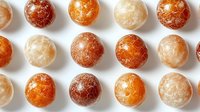 Orange and white round polished aragonite spheres arranged in rows on white background, natural stone crystal balls with marbled patterns and textures.