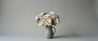 Elegant white and cream roses arranged in rustic ceramic pitcher against soft gray background for home decor and floral design projects.