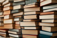Stacks of vintage hardcover books arranged in rows creating textural pattern. Close up view shows worn spines in muted earth tones and blue shades.