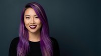 Young Asian woman with vibrant purple hair smiling confidently against dark teal background. Modern portrait for lifestyle and beauty content.