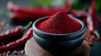 Vibrant red chili powder in black ceramic bowl surrounded by dried red chilies on dark background, dramatic food photography for spicy cuisine and seasoning.