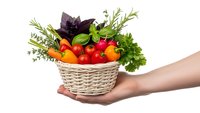 Fresh organic vegetables and herbs in wicker basket held by female hands isolated on white background for healthy cooking and nutrition concepts.