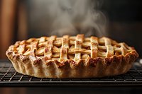 Freshly baked apple pie with golden lattice crust steaming on cooling rack, showcasing traditional homemade pastry with crispy woven top and rustic edges.