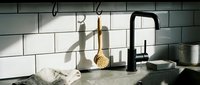 Modern kitchen sink with black matte faucet and white subway tile backsplash. Minimalist design with hanging utensils and natural lighting for home decor.