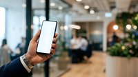 Man holding smartphone with blank screen in modern office lobby, displaying mobile app interface for business communication and technology solutions.