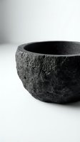 Dark rough-textured stone bowl with rustic carved surface on white background, showcasing natural volcanic rock craft for home decor and kitchen use.