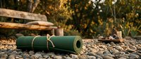 Green yoga mat rolled up on stone surface with wooden bench and autumn foliage background for outdoor fitness and wellness activities.