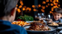 Roasted duck with crispy skin served on dark plate against blurred festive lights background, holiday dinner gathering with wine and warm atmosphere.