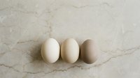 Three fresh chicken eggs in different shades from white to brown arranged on elegant marble surface for cooking and baking projects.