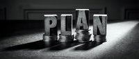 Financial planning concept with metal PLAN letters on stacked coins in dramatic black and white lighting for business and investment strategies.