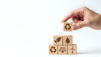 Hand placing wooden cube with recycling symbol on stack of eco-friendly blocks featuring renewable energy icons on white background for sustainable business concepts.