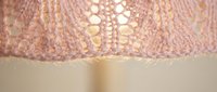 Pink knitted fabric with intricate lace pattern and decorative holes creating delicate texture for crafting and textile design projects.