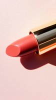 Coral pink lipstick in metallic gold tube casting dramatic shadow on soft pink background. Close-up macro shot highlights luxurious cosmetic texture and shine.
