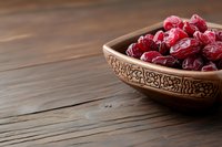 Fresh red dried cranberries in ornate wooden bowl on rustic wood table surface for healthy snacking and cooking ingredients.