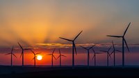 Wind turbines silhouetted against dramatic sunset sky with orange and purple clouds. Renewable energy farm generating clean electricity at golden hour.