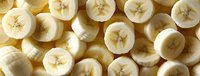 Fresh sliced banana rounds arranged in rows showing cross sections with seeds and creamy flesh, creating natural pattern for healthy food background.