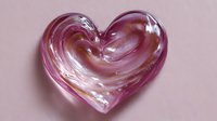 Glass heart in pink and transparent tones with glossy surface and soft shadows on pink background, romantic symbol for love and affection.