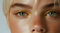 Close-up portrait of young Caucasian woman with striking golden yellow eyeshadow makeup and green eyes, showcasing bold colorful cosmetics trends.