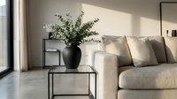 Modern minimalist living room interior with beige sofa, black metal coffee table, eucalyptus plant in ceramic vase, natural sunlight shadows on wall.