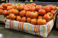 Fresh ripe tomatoes displayed in striped fabric basket at farmers market, showing natural organic produce with vibrant color and texture.