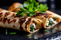 Grilled crepes filled with fresh spinach and cheese mixture, garnished with parsley on dark stone background. Close up view of homemade savory pancakes.