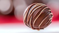 Gourmet chocolate truffle with elegant white chocolate drizzle on blurred red background, perfect for dessert menu or confectionery advertising.