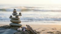 Balanced stone cairns on driftwood at peaceful ocean beach with soft waves and sandy shore creating zen meditation atmosphere for wellness and mindfulness concepts.