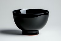 Elegant black ceramic bowl with glossy finish on white background, casting soft shadow. Minimalist Asian-inspired tableware design for modern dining presentation.