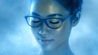 Young Asian woman with glasses and gentle smile in dreamy blue atmosphere, eyes closed in peaceful meditation. Ethereal lighting creates serene wellness mood.