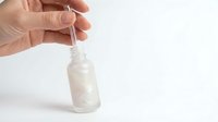 Hand holding glass dropper bottle with white serum or oil on clean background for skincare and beauty product marketing.
