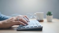 Professional hands typing on modern keyboard at clean workspace with coffee cup and succulent plant for productivity and office work concepts.