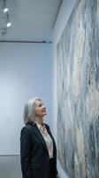 Mature Caucasian businesswoman in dark suit admiring large abstract painting in modern art gallery with white walls and professional lighting.
