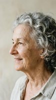 Elderly Caucasian woman with curly gray hair smiling in profile, natural light, neutral background, aging gracefully concept.