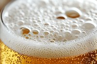 Extreme close-up of fresh beer foam and bubbles on golden amber liquid, showing detailed texture and carbonation in macro photography for beverage advertising.
