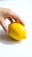 Hand holding a fresh ripe yellow lemon on white background, close-up shot for food, health, and nutrition concepts.